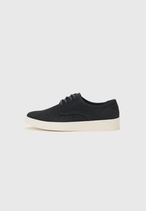 Chaussure en daim noir à lacets avec un bout arrondi, semelle légère crème et subtils accents de coutures bleues sur la tige.