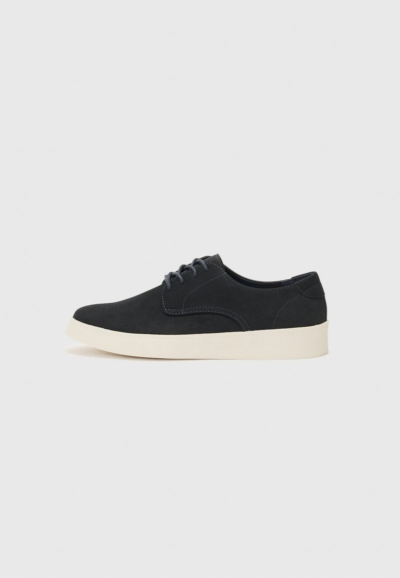 Zapato negro de ante con cordones, punta redonda, suela ligera de color crema y sutiles acentos de costura azul en la parte superior.