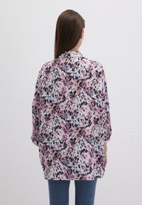 Blumenbluse mit lockerem Schnitt, featuring pinken, lilanen und blauen Mustern auf einem hellen Hintergrund. Weicher Stoff, Dreiviertelärmel.