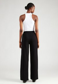 Zwarte wijde broek met een hoge taille, gecombineerd met een aansluitend wit tanktop. De stof lijkt glad met een minimale textuur.