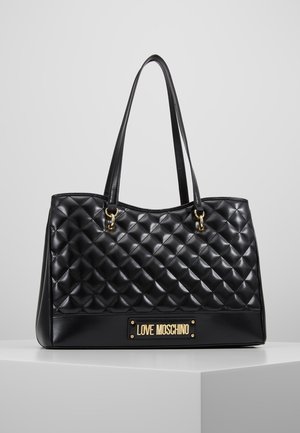Czarna pikowana skórzana torba typu tote z podwójnymi uchwytami i złotą plakietką z logo "LOVE MOSCHINO" z przodu, prezentowana na białym piedestale.