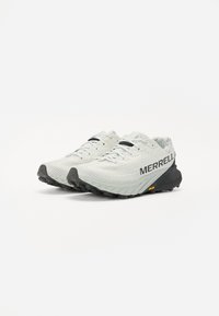 Baskets de trail de course gris clair avec une tige texturée, des accents noirs et une semelle extérieure noire robuste. Présente la marque "MERRELL" sur le côté.