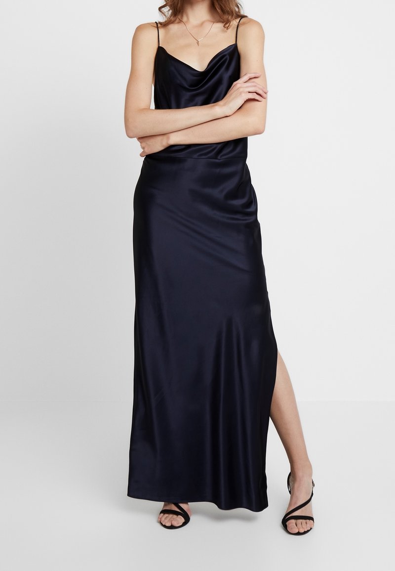 Robe longue en satin bleu marine avec un col bénitier, des bretelles fines et une fente latérale. La texture lisse met en valeur le drapé élégant et la silhouette.
