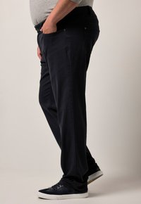 Pantalones azul marino en mezcla de algodón, de corte relajado con bolsillos laterales, cierre de botón, combinados con zapatillas oscuras, vista lateral visible.