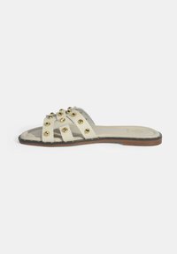 Open-toe slide sandaal in crème synthetisch materiaal. Beschikt over meerdere banden met gouden studs, een gestructureerde binnenzool en een platte bruine zool.