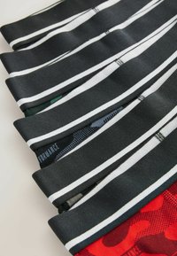 Shorts de performance noirs avec des rayures blanches, présentant un mélange de styles et de motifs, y compris des motifs camouflage et géométriques, pliés avec soin.