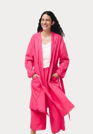 Růžový loungewear set, který obsahuje dlouhý župan s kapsami a odpovídající zkrácené kalhoty, vyrobený z lehké, texturované látky s jemnými vzory.