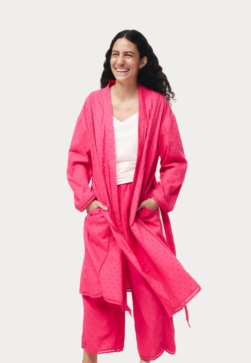Set di abbigliamento da casa rosa composto da un lungo accappatoio con tasche e un pantalone corto coordinato, realizzato in un tessuto leggero e testurizzato con motivi sottili.