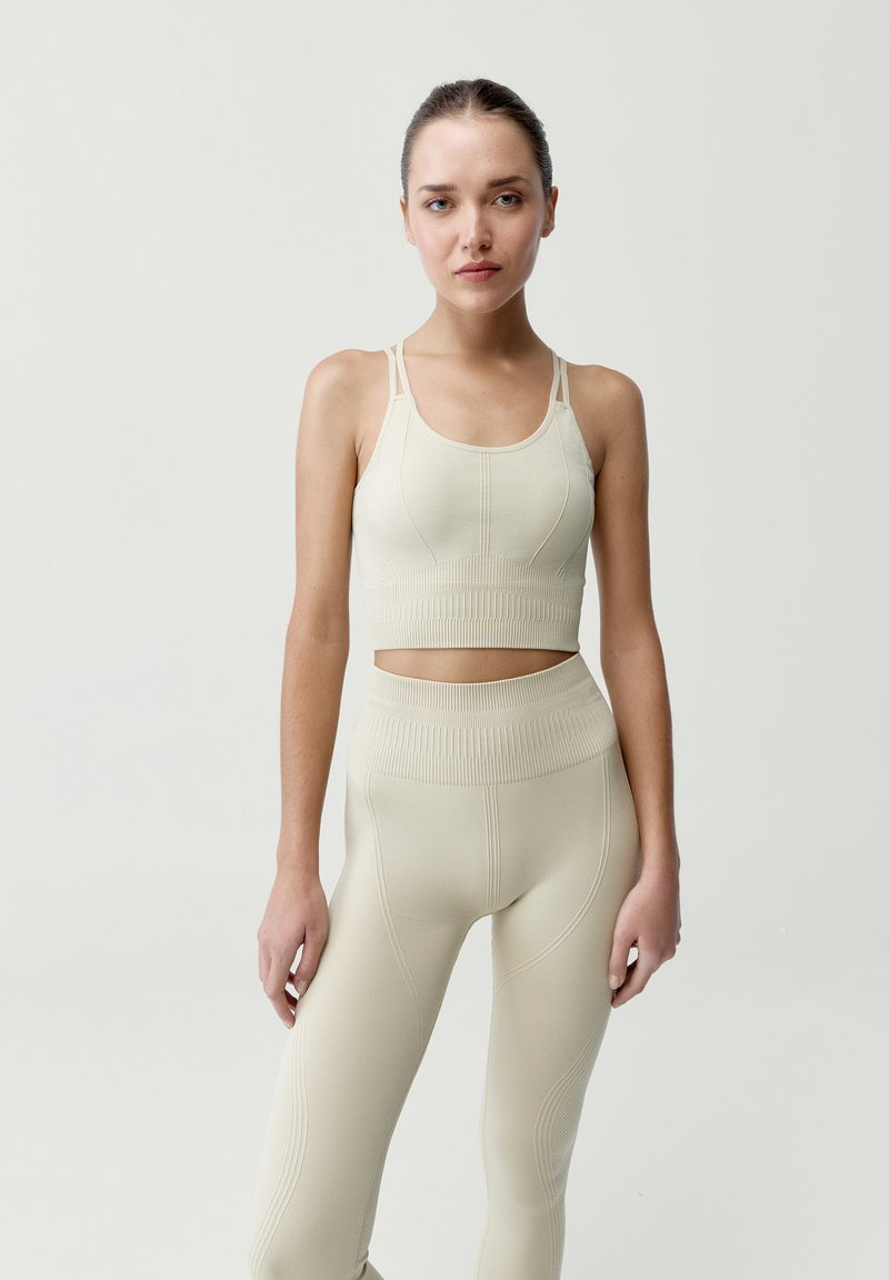 Béžový sportovní top na krátké rukávy a odpovídající vysoké legíny, které mají žebrovanou strukturu a švy pro dokonalé přizpůsobení.