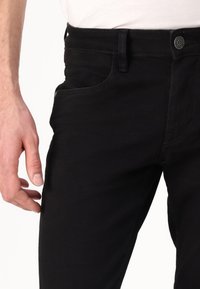 Vaqueros de denim negro con corte ajustado, que presentan un diseño de cinco bolsillos, cremallera y costuras negras. La tela tiene una textura suave.