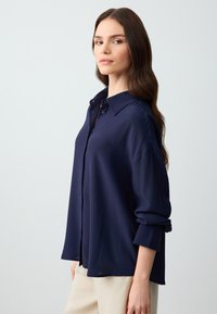 Marineblauwe button-up shirt in een lichte stof met een kraag en opgerolde mouwen, met een losse pasvorm en een subtiele textuur.