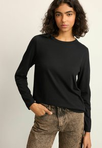 Sort langærmet skjorte lavet af blødt stof, med en rund hals og en let afslappet pasform, parret med mønstrede brune jeans.