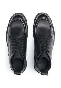 Zwarte leren schoenen met een ronde neus, zes oogjes voor veterdoek, textuur in het oppervlak en een trekhaak aan de hiel.