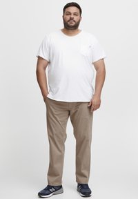 White cotton T-shirt with short sleeves and a chest pocket, paired with light brown chinos and navy athletic shoes.