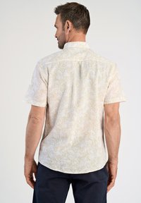 Camicia a maniche corte color beige chiaro con un sottile motivo floreale e tessuto testurizzato, dotata di colletto rialzato e orlo dritto.