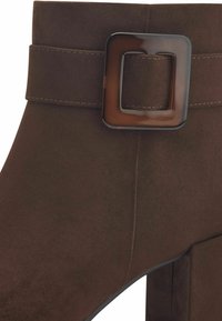 Brown suede ankle boot with a square buckle detail. Features a sturdy heel and smooth texture, emphasizing a tailored design.