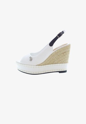 Sandalia de cuña blanca tipo slingback con tacón de yute trenzado, diseño de punta abierta y un pequeño acento decorativo en la parte superior. Detalle de correa negra.
