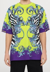 Tričko s krátkým rukávem s výrazným žlutým a fialovým designem, modrými květinovými vzory a pruhy zebry. Bavlněný materiál, volný střih.