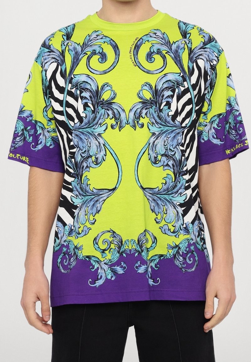 Tričko s krátkým rukávem s výrazným žlutým a fialovým designem, modrými květinovými vzory a pruhy zebry. Bavlněný materiál, volný střih.