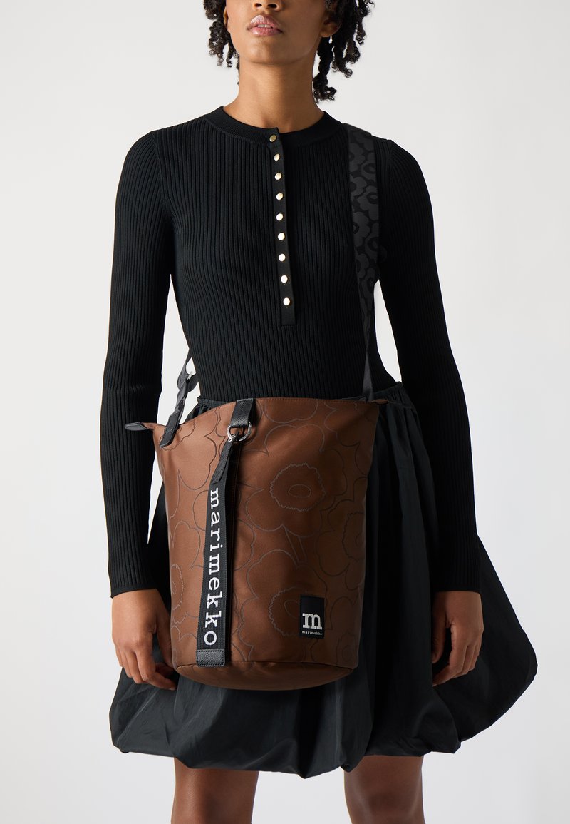 Borsa a tracolla marrone con motivo floreale e dettagli neri. Presenta spallacci regolabili e logo 'marimekko' sul lato. Materiale testurizzato e resistente.