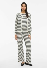 Set di loungewear a righe in crema e nero, composto da un cardigan a maniche lunghe e pantaloni a gamba larga, realizzato in un tessuto morbido. Scarpe basse.