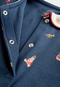 Dunkelblaues Baumwoll-Polohemd mit bunten Druckmotiven von Spielzeug, Trompete und Trommel. Enthält silberne Druckknöpfe und einen rot akzentuierten Kragen.
