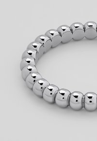 Sølvfarget metallarmbånd med en serie av glansfulle, runde perler med en glatt tekstur og små hull, arrangert i et fleksibelt bånd.