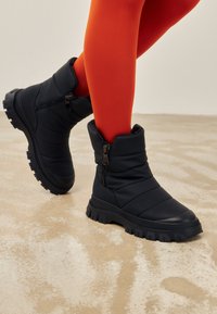 Zwarte gevoerde enkellaarsjes met een zijrits, dikke rubberen zool en een gestructureerde afwerking, gecombineerd met felrode maillots.