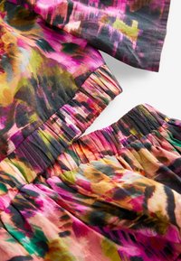 Farbiger Stoff mit einem Blumenmuster in Rosa-, Orange- und Grüntönen sowie gerafften elastischen Details. Leichtes, strukturiertes Material.