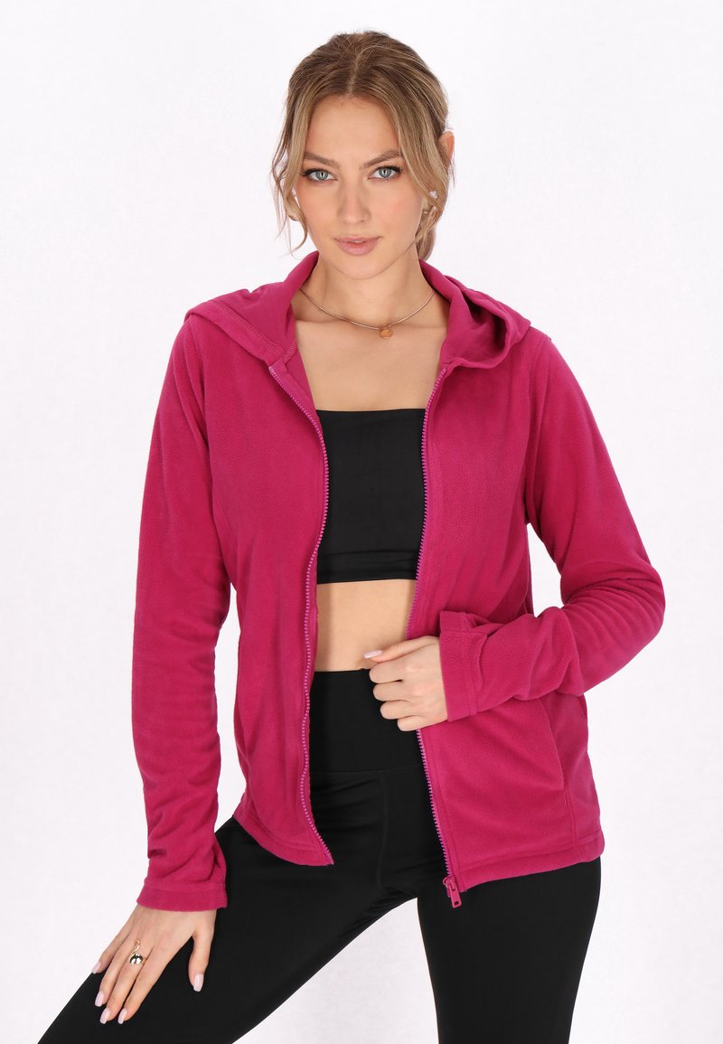 Fleece zip-up huppari kirkkaassa magentassa, jossa on nyörillä säädettävä huppu, pitkät hihat ja yksi sivutasku, yhdistetty mustaan crop topiin.