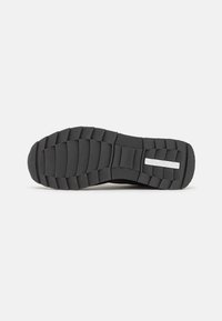 Semelle de sneaker noire en caoutchouc texturé, avec des rainures horizontales et verticales pour une meilleure adhérence. Section médiane lisse avec un détail de marque.