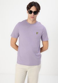 T-shirt en coton lilas avec col rond et un petit logo jaune brodé sur le côté gauche de la poitrine. Manches courtes et coupe régulière.