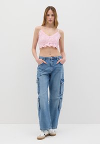 Top corto all'uncinetto rosa con spalline sottili, abbinato a jeans cargo a gamba larga azzurri chiari con tasche laterali. Sneakers bianche completano il look.