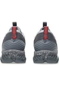 Scarpe sportive grigie con tomaia in rete testurizzata, accenti rossi e un intersuola maculata, caratterizzate da un design distintivo della suola ondulata.