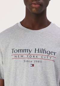Grå bomulds T-shirt med "Tommy Hilfiger New York City" tryk i marineblå og rød. Rund hals og korte ærmer, med logo accent.