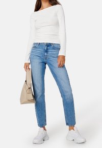 Witte lange mouw top met een off-shoulder ontwerp, gecombineerd met medium-wash blauwe jeans en witte sneakers. Beige tas met knoopdetail.