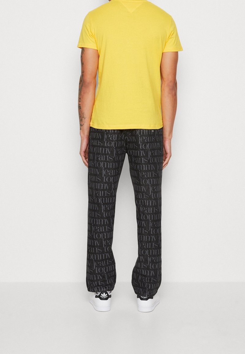 Yellow short-sleeve t-shirt paired with black pants featuring a repeated text pattern. White sneakers complete the outfit.