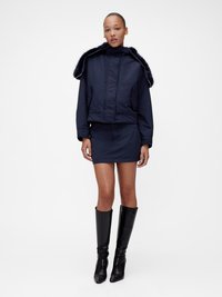 Μπλε σκούρο cropped σακάκι με ψεύτικο γούνινο γιακά, σε συνδυασμό με μίνι φούστα στο ίδιο χρώμα και μαύρες μπότες μέχρι το γόνατο. Λείο ύφασμα και εφαρμοστή γραμμή.