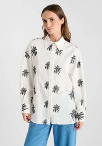 White button-up shirt made of lightweight fabric, featuring black palm tree prints, long sleeves, and a standard collar.
