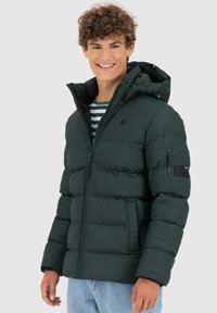 Giacca puffer verde scuro con texture trapuntata, chiusura con zip, cappuccio staccabile e tasca con zip sul braccio sinistro.