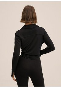 Haut noir à manches longues en tissu doux et extensible, avec un col, un ourlet arrondi et une silhouette ajustée. Détails texturés au dos.