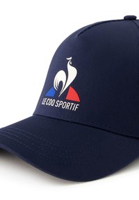 Gorra de béisbol navy hecha de algodón con visera curva, que presenta un logo de gallo blanco y formas de acento en rojo y azul en la base.