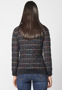 Fitted zwart sweater met meerkleurige geweven strepen, textuur stof, lange mouwen en geribde manchetten. De lengte reikt tot de heupen.