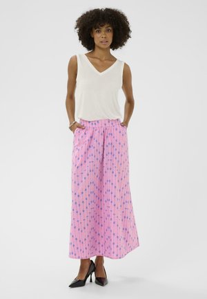 Femeie cu păr creț, purtând un top alb fără mâneci, pantaloni roz cu imprimeu albastru, talie înaltă și largi, și pantofi negri cu toc înalt.