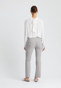 Weiße Bluse mit Halsband, kombiniert mit hellgrauen, taillierten Hosen und gemusterten Slidern. Glatter Stoff und entspannte Passform. Minimalistisches Design.