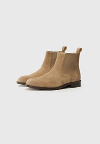 Bottines Chelsea en suede marron clair avec des panneaux latéraux élastiques, des anses de tirage, des orteils ronds et un talon bas, plat. Texture lisse sur toute la surface.