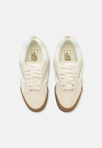 Cream sneakers with a smooth texture, featuring a white tongue, beige laces, and a brown rubber sole. Minimalist design with blue accents.