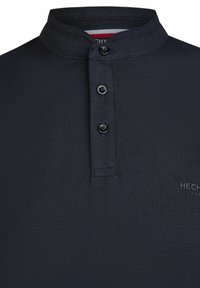 Navy Polo-Shirt mit Stehkragen, ausgestattet mit drei schwarzen Knöpfen und einem strukturierten Stoff. Logo in Schwarz auf der unteren rechten Seite.