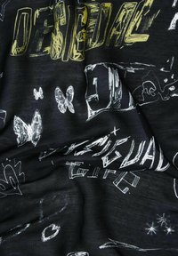 Mustan kankaan pinta, jossa on valkoisia ja keltaisia abstrakteja piirustuksia, mukaan lukien perhosia ja kirjaimia, pehmeä ja teksturoidun tuntuinen pinta.