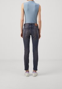 Ljusblå ärmlös topp, mörkblå skinnyjeans och vita sneakers med lavendelaccenter, som visar upp en figurnära siluett och en avslappnad stil.